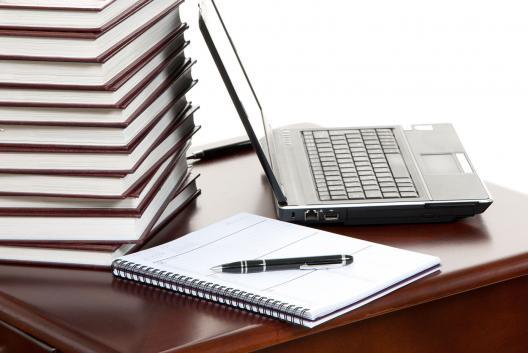 stack of books, a laptop, a notepad, and a pen laying on a desk