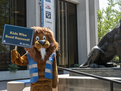 The State Library mascot Dewey with a Children who read, exceed sign.
