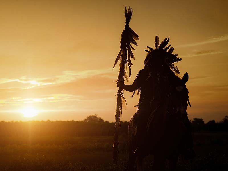 Silhouette of a Native American as the sun sets behind him.