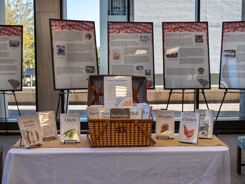 Photo of the exihibit South Carolina: The Food We Celebrate shoiwing a table with a selection of books on different southern foods, and easel displays behind describing different southern food traditions.