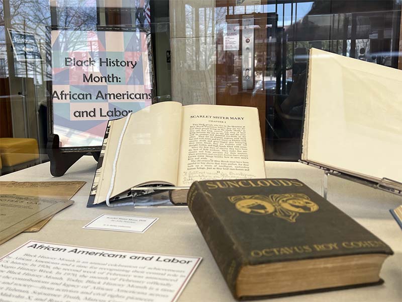 Selected books in the State Library's display case from the A.S. Salley Collection. One book closed, one open, and a sign behind them stating Black History Month: African Americans and Labor