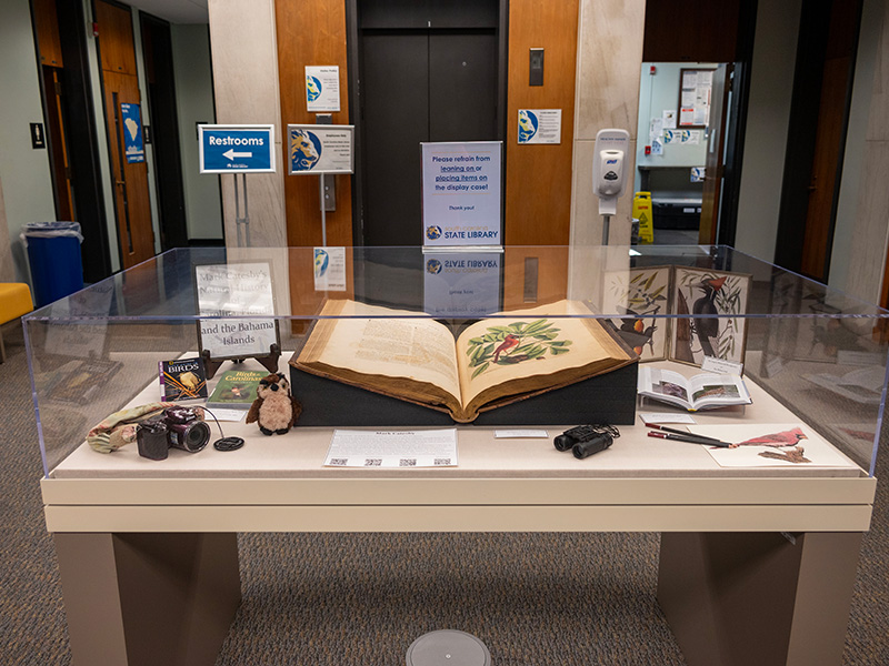 Image of the display case in the SCSL lobby with the Mark Catesby book open to an illustration of a cardnial.