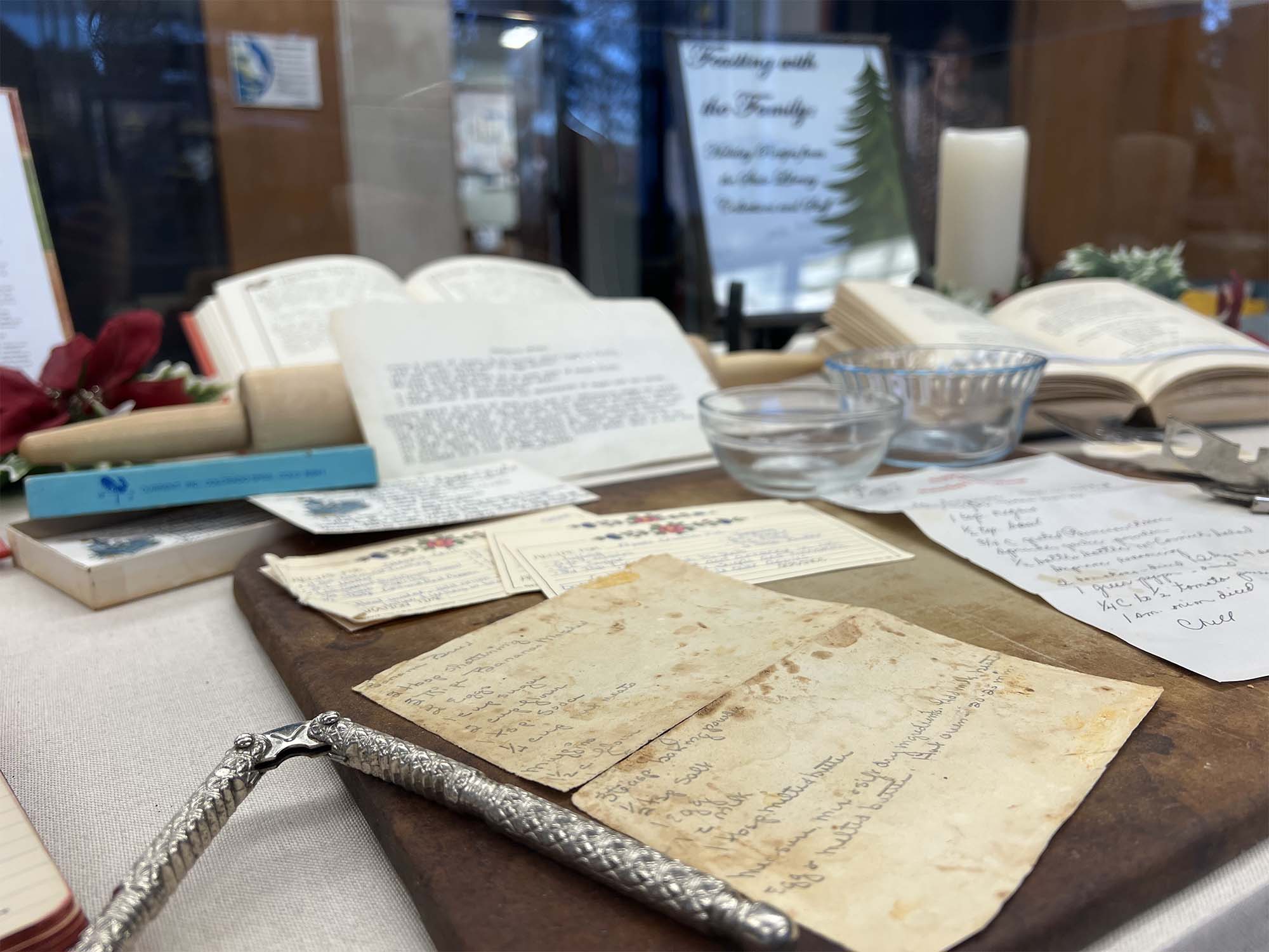 A selection of handwritten and typewritten recipes in our glass display case with some kitchen utensiles and Christmas ribbon surrounding them