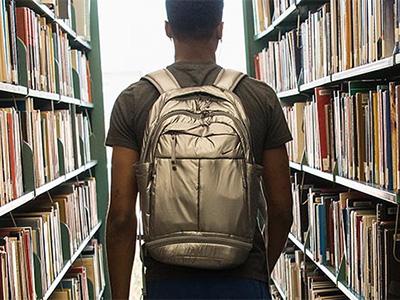 Student walking through the stacks of a library, seen from behind.