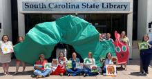 staff members holding up giant green caterpillar and eric carle books